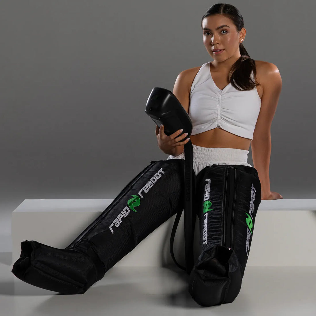 Athletic woman wearing a white Upper and White Trouser using Rapid reboot therapy boots.