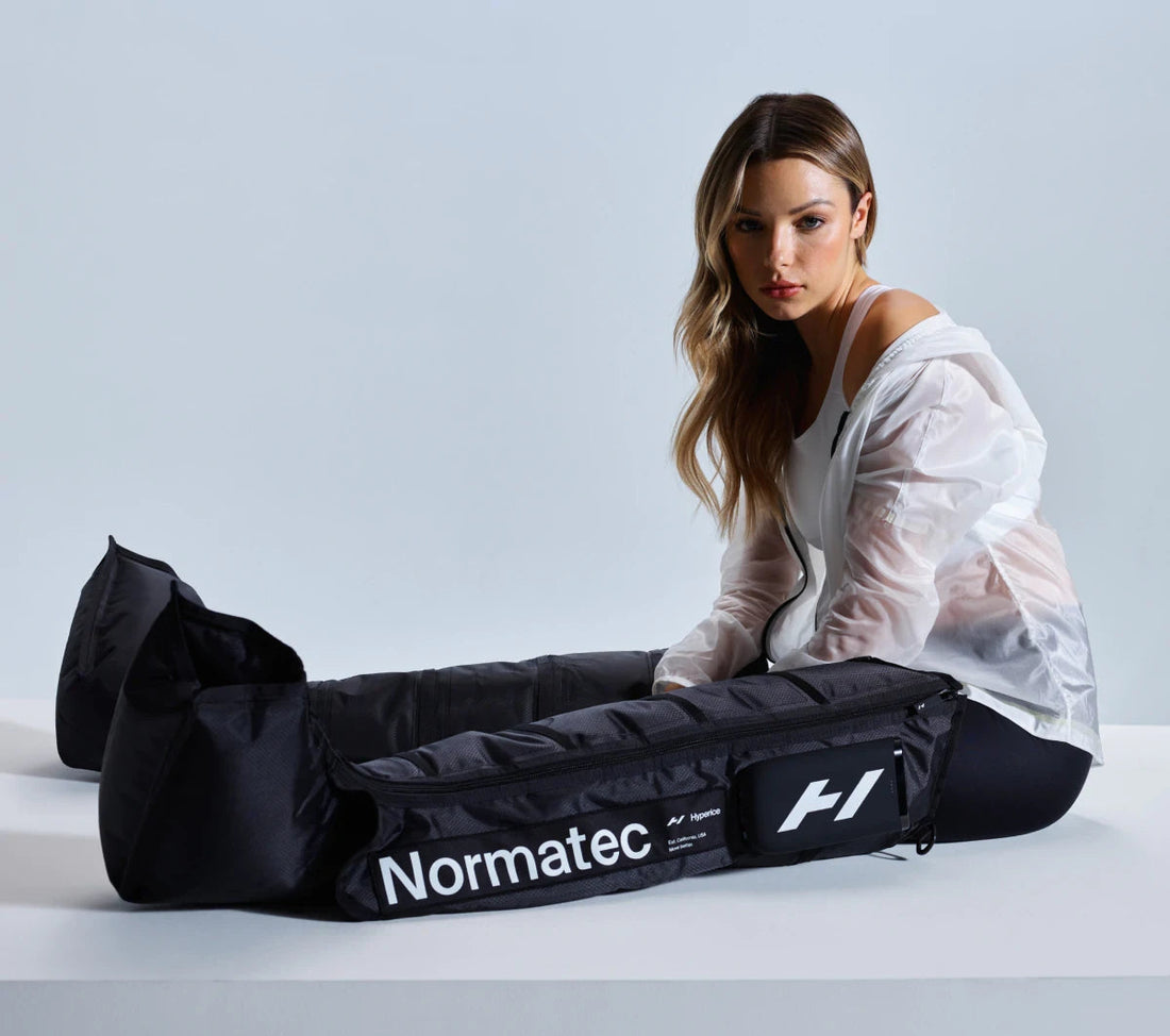 Athletic woman wearing a white jacket and black leggings using Normatec compression therapy boots.